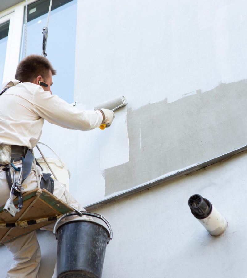 Builder-alpinist paints the facade of the building in a light color